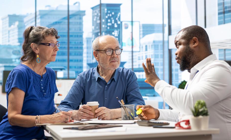 Three people sit at a desk in a work discussion