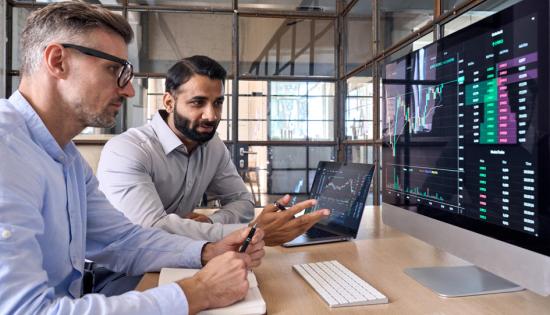 Two men at a desk looking at data on a computer screen